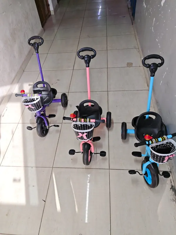 Three kids' push tricycles in purple, peach and blue, each with a push handle and a front basket